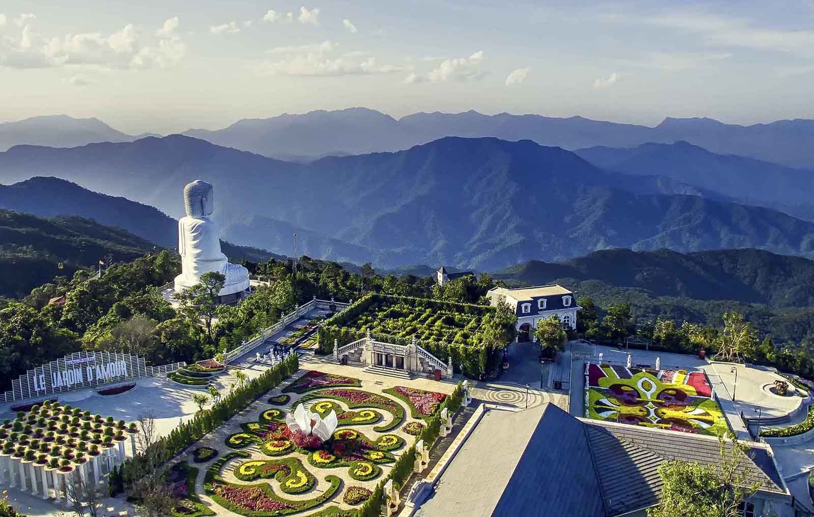 A tall white Buddha statue beside a pagoda on a green mountainside