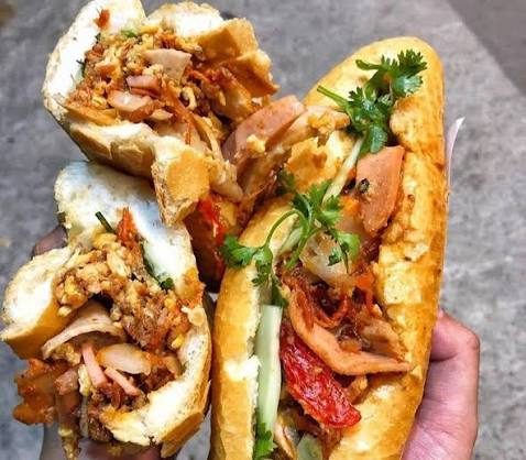 Two Vietnamese banh mi sandwiches held up, filled with pork and herbs
