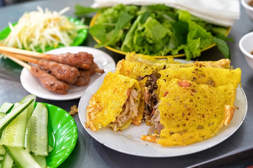 Crispy banh xeo pancake served with grilled pork skewers and fresh herbs