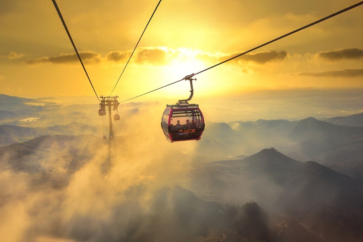 A cable car gondola silhouetted against a sunset over the mountains
