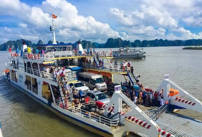 A car and passenger ferry with limestone karsts behind, on the way to Cat Ba Island