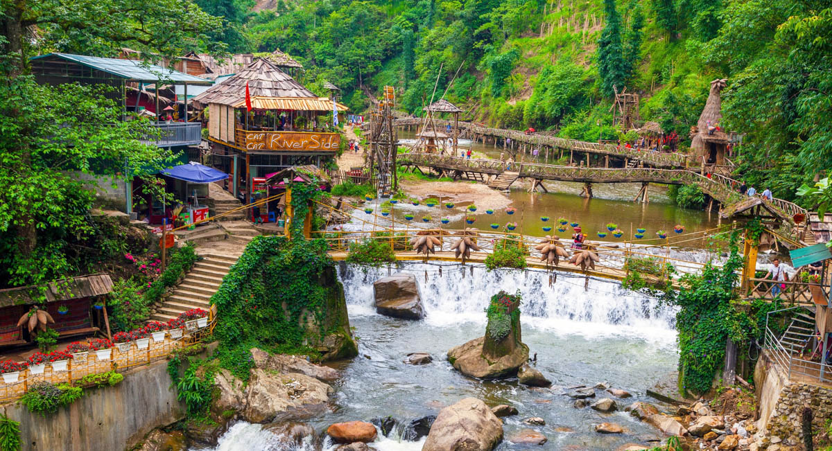 Wooden houses and a waterfall with a small bridge in Cat Cat village, Sapa