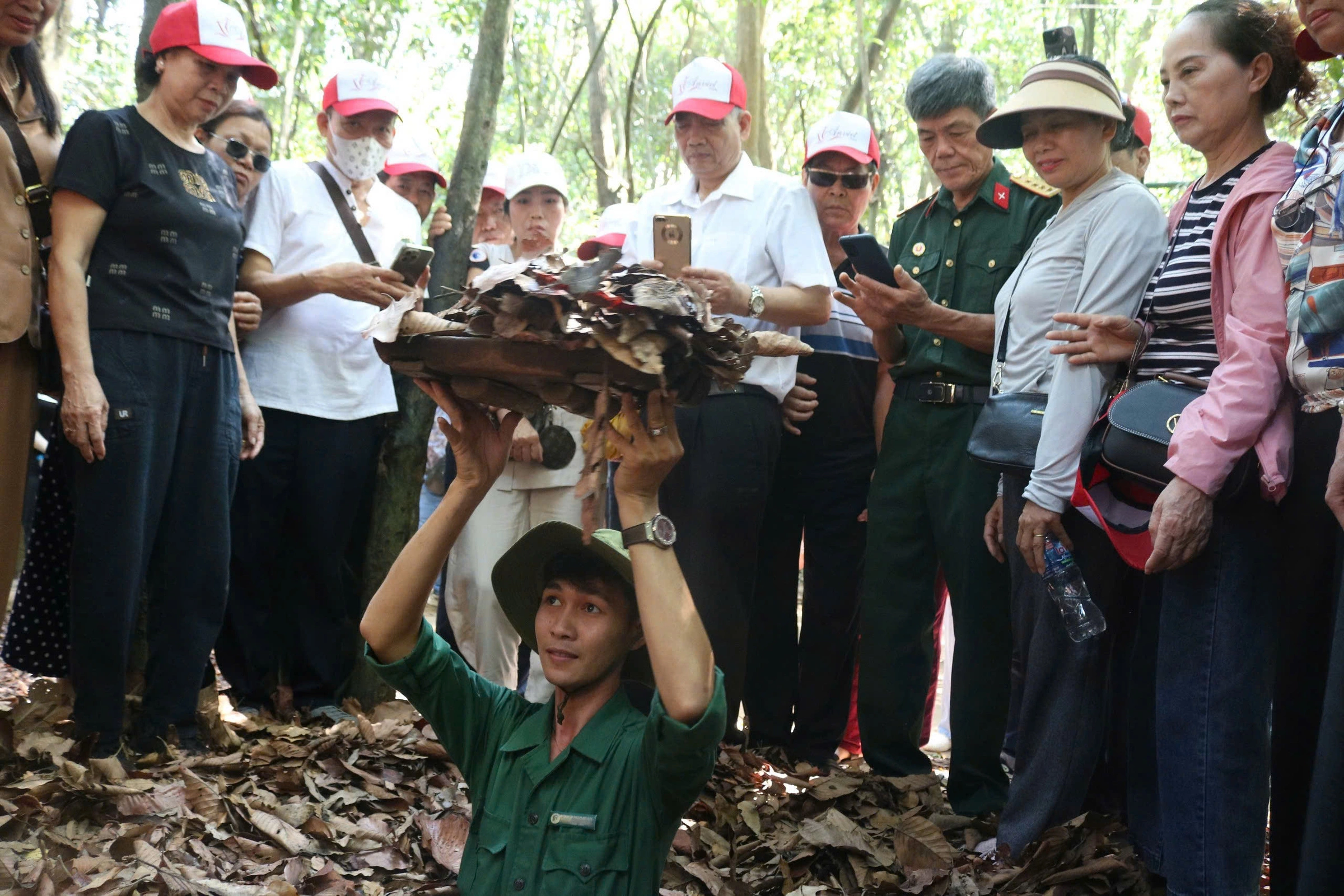 A guide showing a hidden camouflaged tunnel entrance at the Cu Chi Tunnels