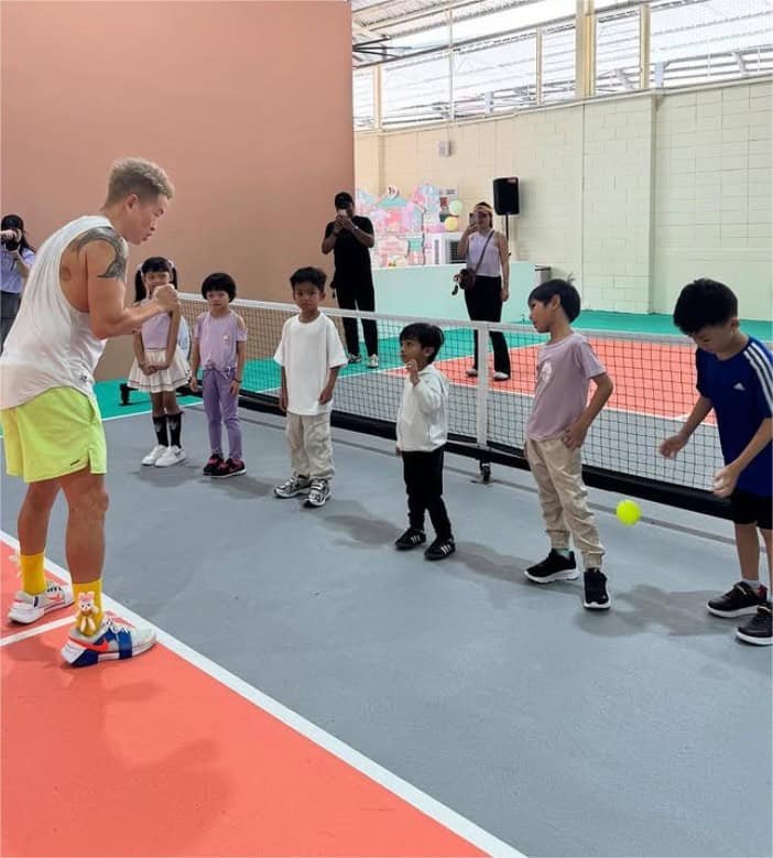A coach showing a group of young children how to play pickleball on an indoor court