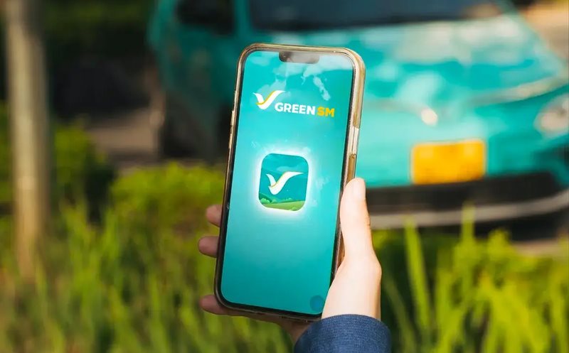 A phone opening the Green SM app in front of a green electric taxi in Vietnam