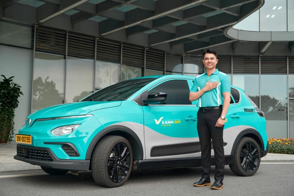 A uniformed driver beside his Green SM (Xanh SM) electric taxi at an airport in Vietnam