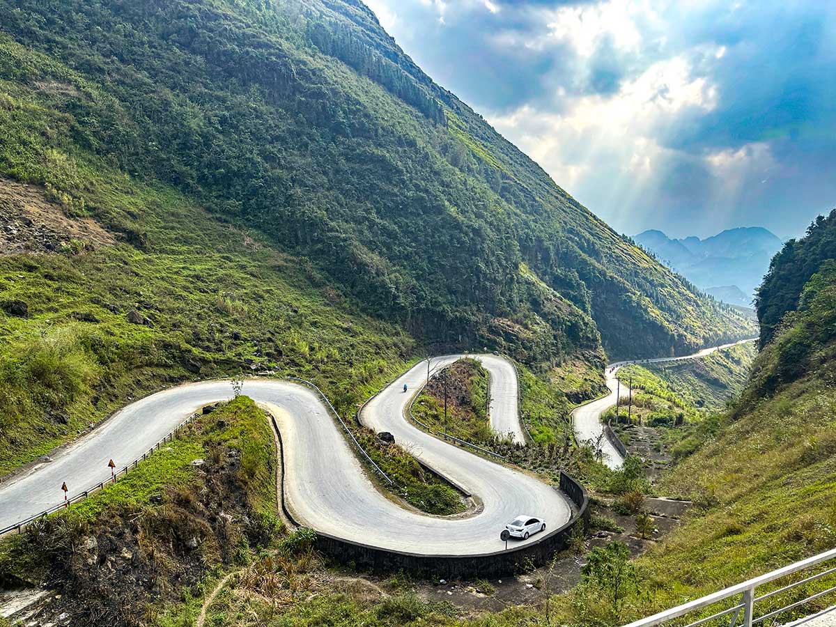 A hairpin mountain road winding through the valleys of the Ha Giang Loop