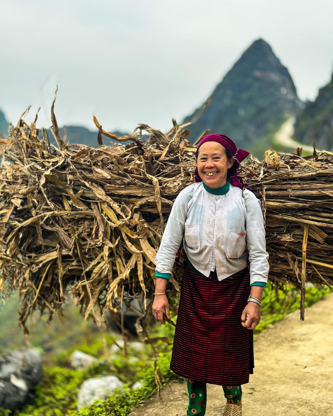 A woman from an ethnic minority community carrying firewood along a mountain road in Ha Giang