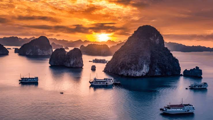 Sunset over limestone karsts and cruise boats in Ha Long Bay