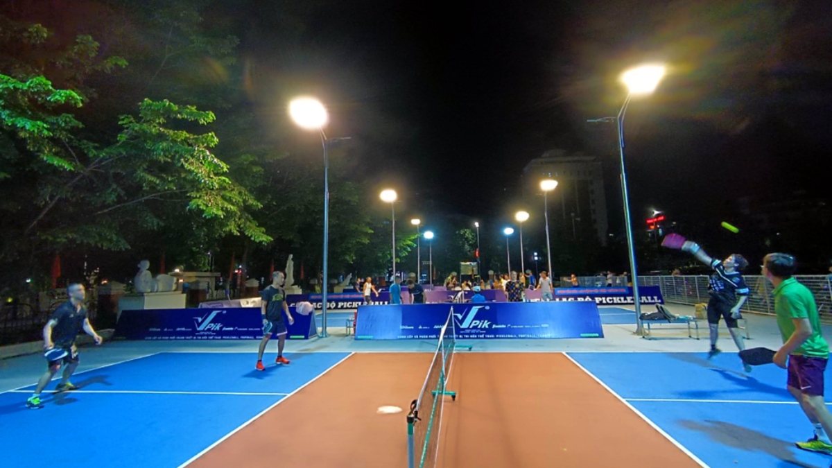 Local players in a doubles game on a floodlit outdoor pickleball court in Hanoi in the evening