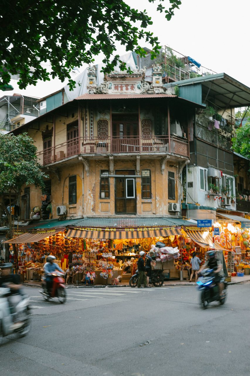 A classic yellow colonial corner building in Hanoi Old Quarter with shops and scooters