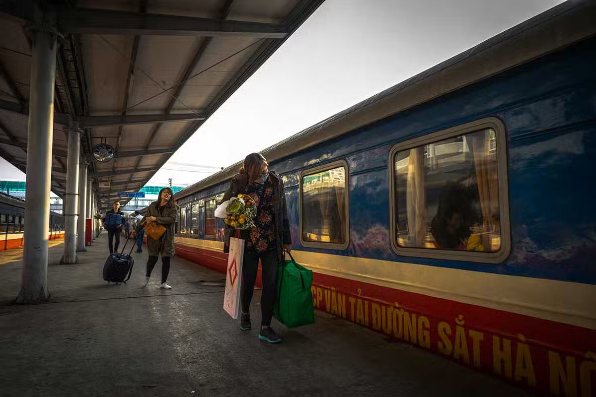 Passengers with luggage beside a blue Vietnam Railways train on the platform at Hanoi Station