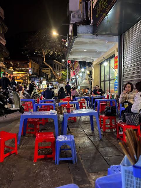 People eating street food on low plastic stools on a Hanoi street in the evening
