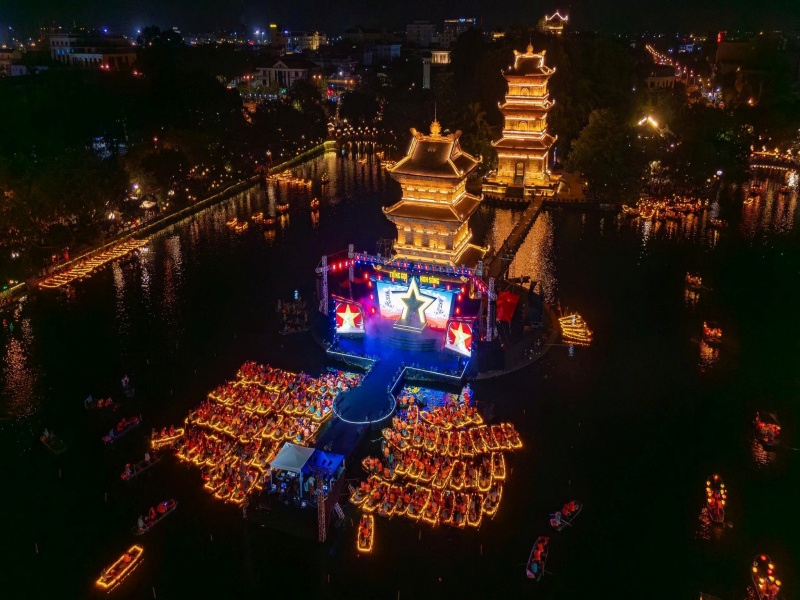 Hoa Lu old town at night from above, with lantern boats gathered around a lit stage on Ky Lan Lake
