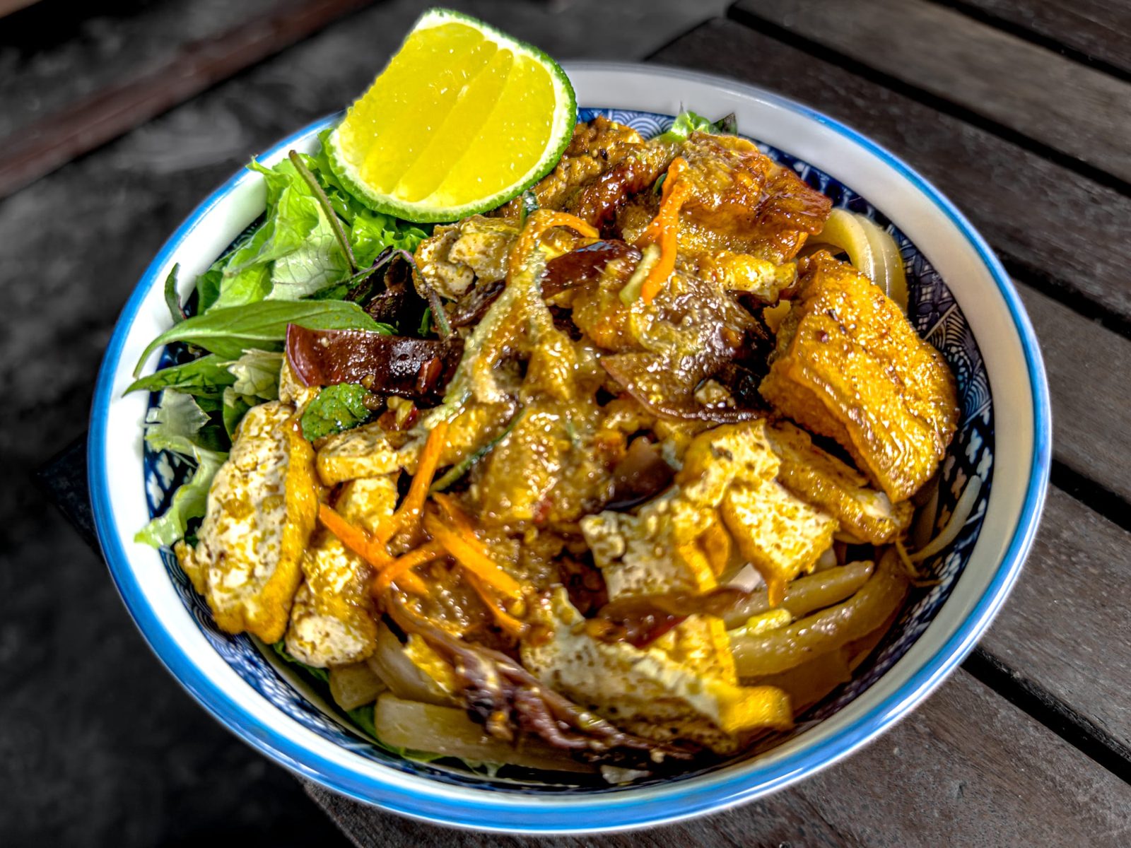 A bowl of vegan cao lau noodles with tofu and herbs in Hoi An