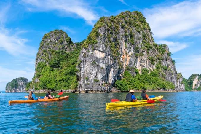 Kayaks on calm green water between limestone islands in Lan Ha Bay