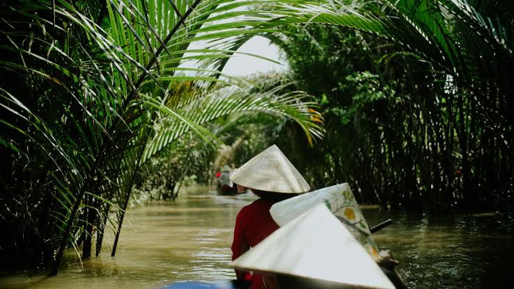 A woman in a conical hat rowing a small wooden boat on the Mekong River