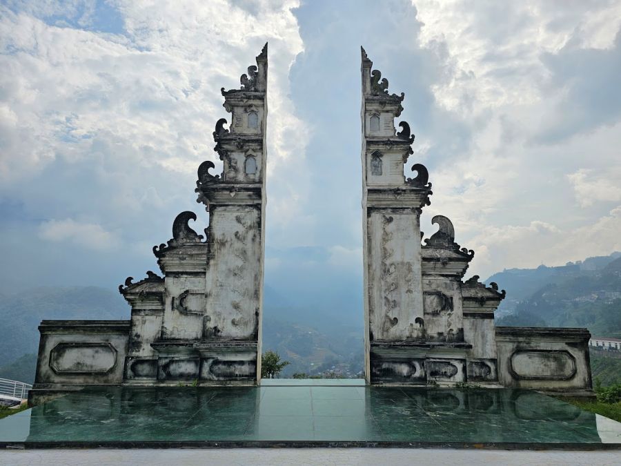 A carved gate photo spot on a mirrored floor overlooking mountains at Moana Sapa