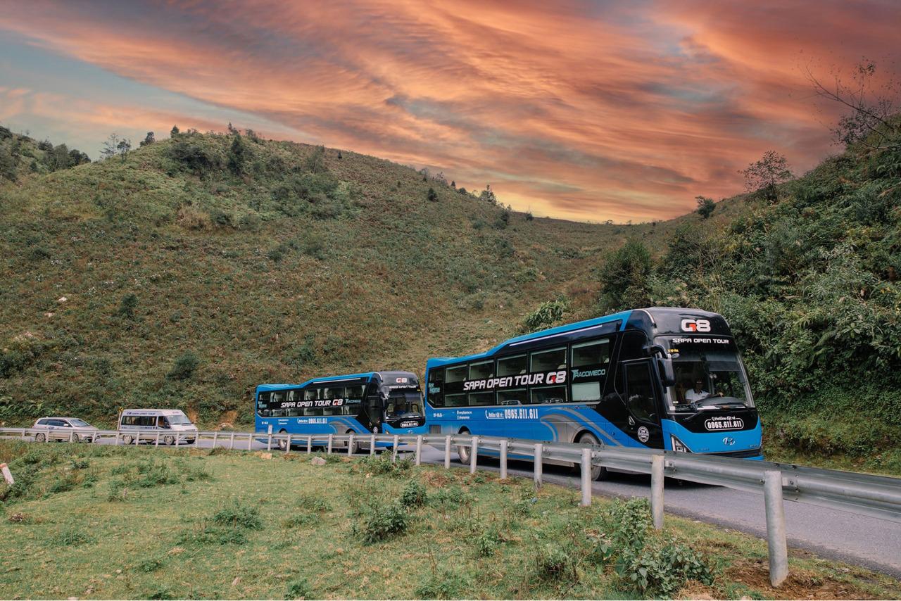 A minibus driving along a mountain road through green hills in northern Vietnam