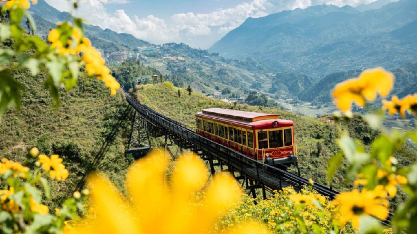A red mountain train crossing a viaduct above rice terraces in the Muong Hoa valley