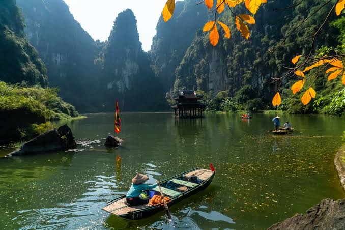 A small rowing boat on the Trang An river between limestone cliffs in Ninh Binh
