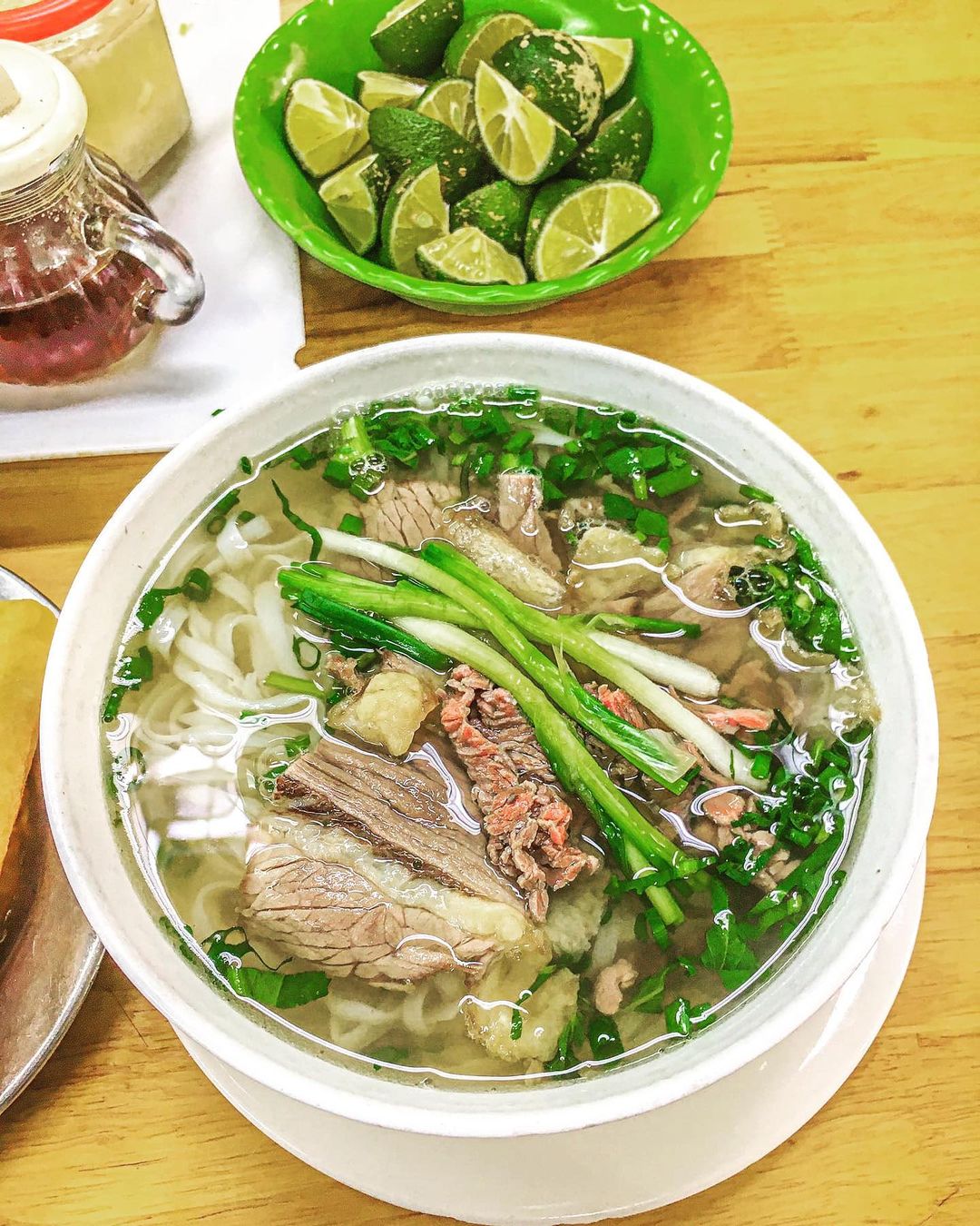 A bowl of Hanoi-style beef pho with fresh herbs, lime and chili