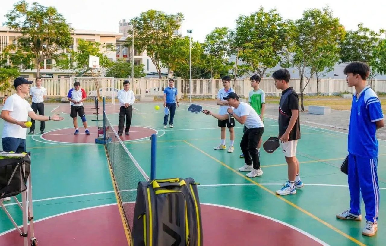 A coach teaching a group of beginners on an outdoor pickleball court in Da Nang