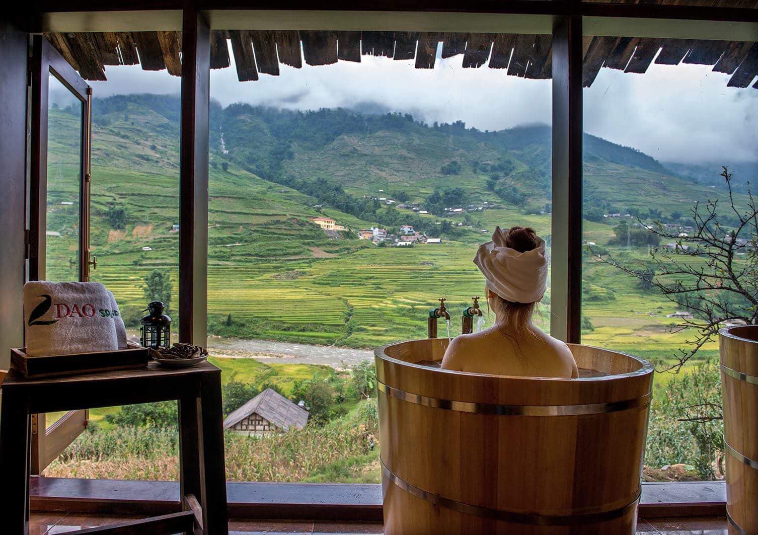 A wooden tub filled with steaming dark herbal water and fresh leaves