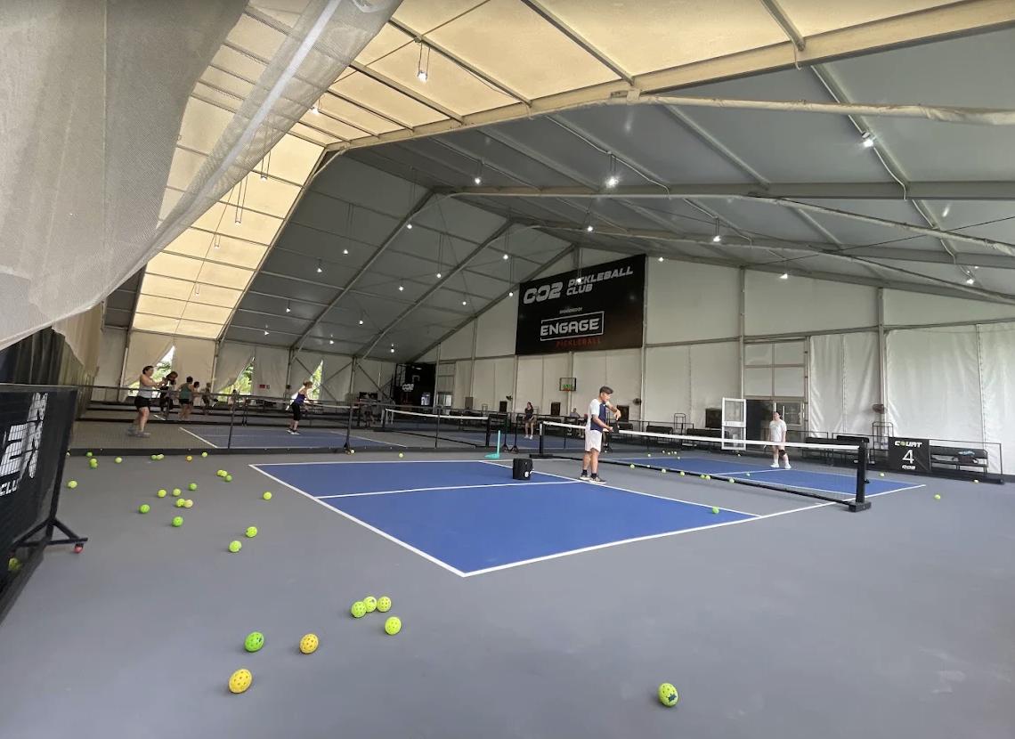 Players on indoor pickleball courts under a high roof with fans in Ho Chi Minh City