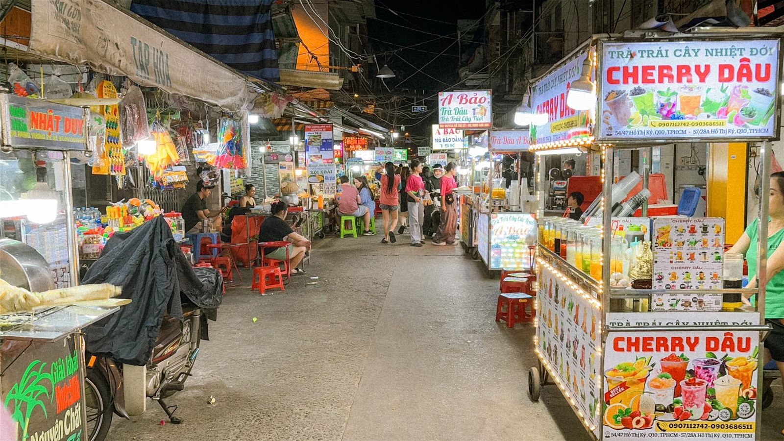 Street food stalls and diners on plastic stools on a busy street in Ho Chi Minh City at night