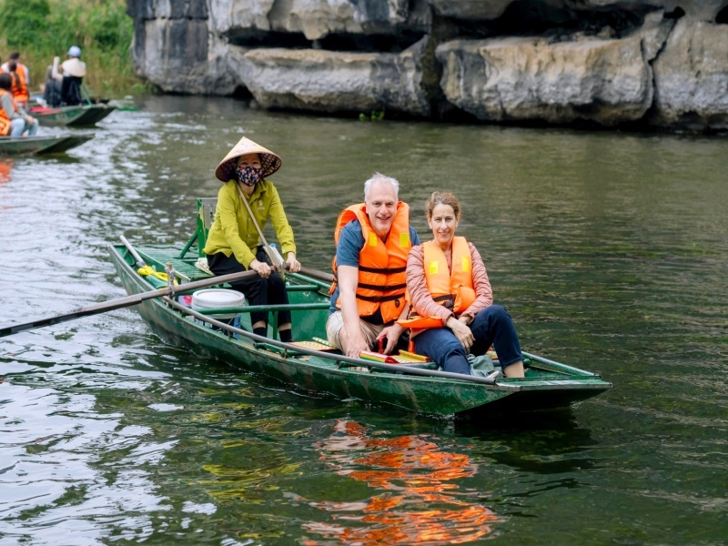 A local woman rowing a small boat through rice fields and limestone hills at Tam Coc
