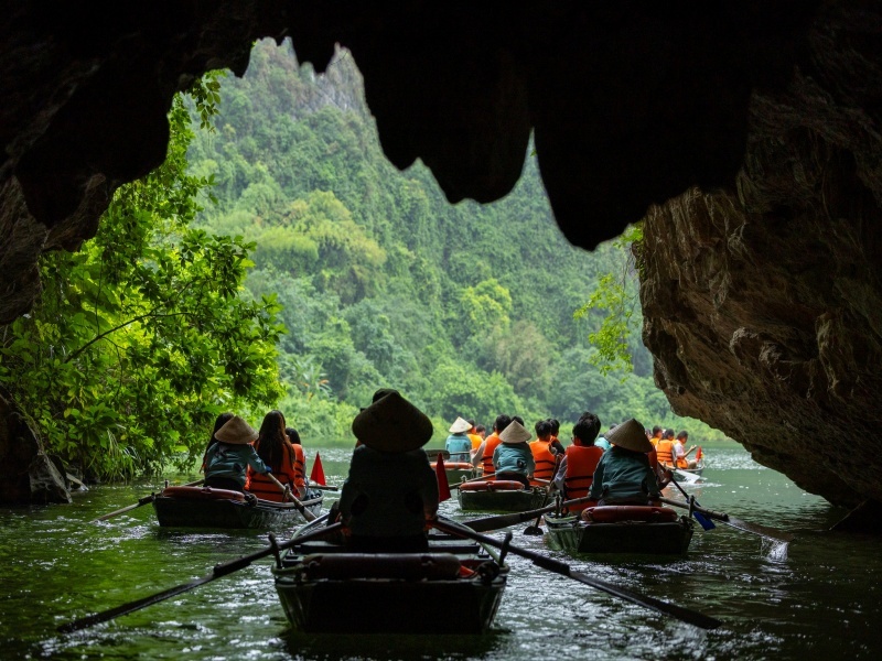 Rowboats with visitors in orange life jackets at the mouth of a cave on the river at Trang An, Ninh Binh