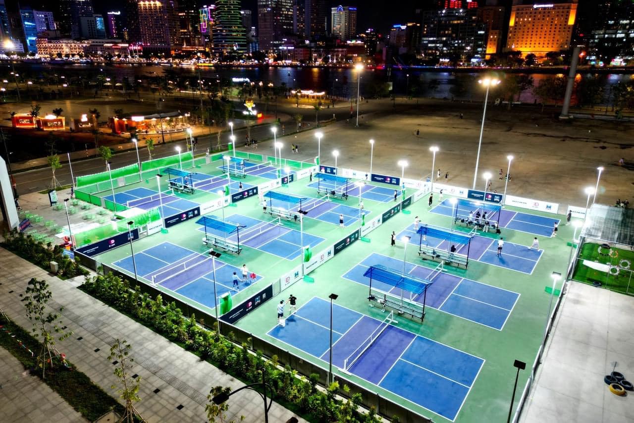 A row of floodlit outdoor pickleball courts full of players at a club in Vietnam at night