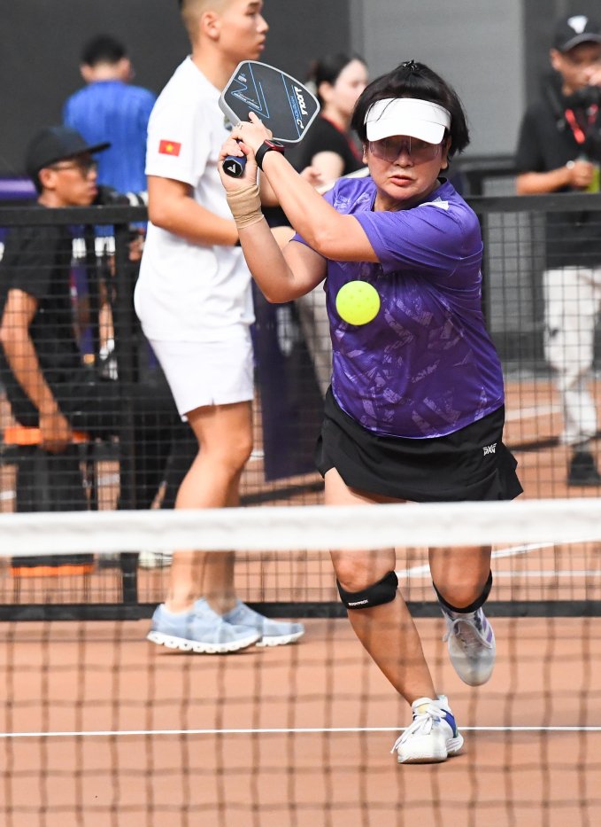 A woman over 50 in a sun-protective top and skort playing pickleball in Vietnam