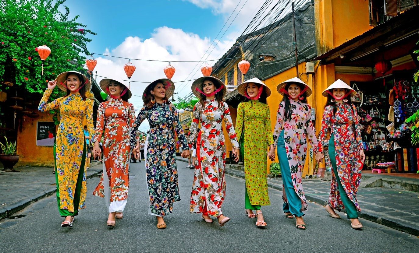 Women in traditional ao dai walking a lantern-strung street in Hoi An Old Town